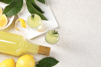 Photo of Tasty limoncello liqueur, lemons and green leaves on light textured table, flat lay. Space for text