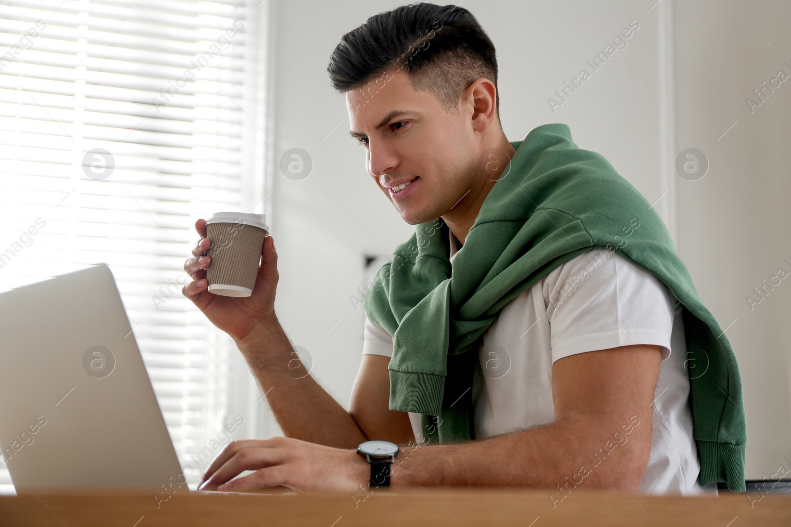 Photo of Freelancer with cup of coffee working on laptop at table indoors