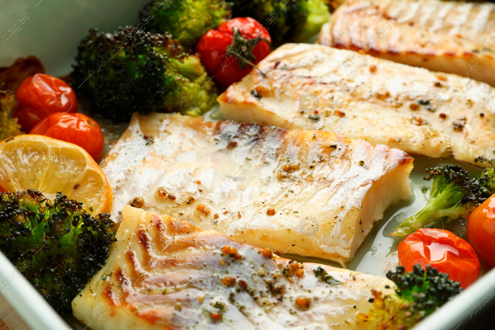 Photo of Pieces of delicious baked cod with vegetables and spices in dish, closeup