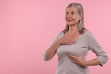 Beautiful senior woman doing breast self-examination on pink background, space for text