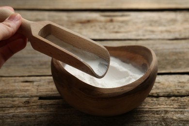 Photo of Woman taking baking powder with scoop from bowl at wooden table, closeup