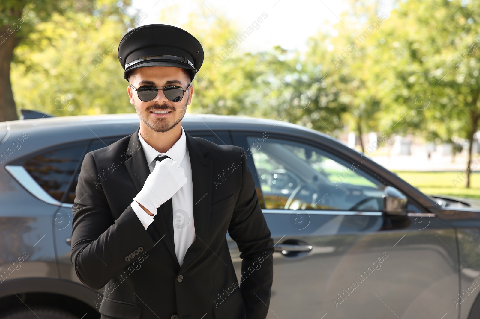 Photo of Young handsome driver standing near luxury car. Chauffeur service