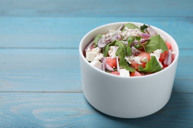 Photo of Delicious salad with watermelon, red onion, arugula and feta cheese on light blue wooden table. Space for text