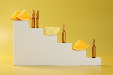 Photo of Stylish presentation of skincare ampoules with vitamin C and citrus slices on yellow background
