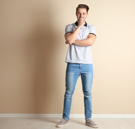 Young man in stylish jeans near light wall