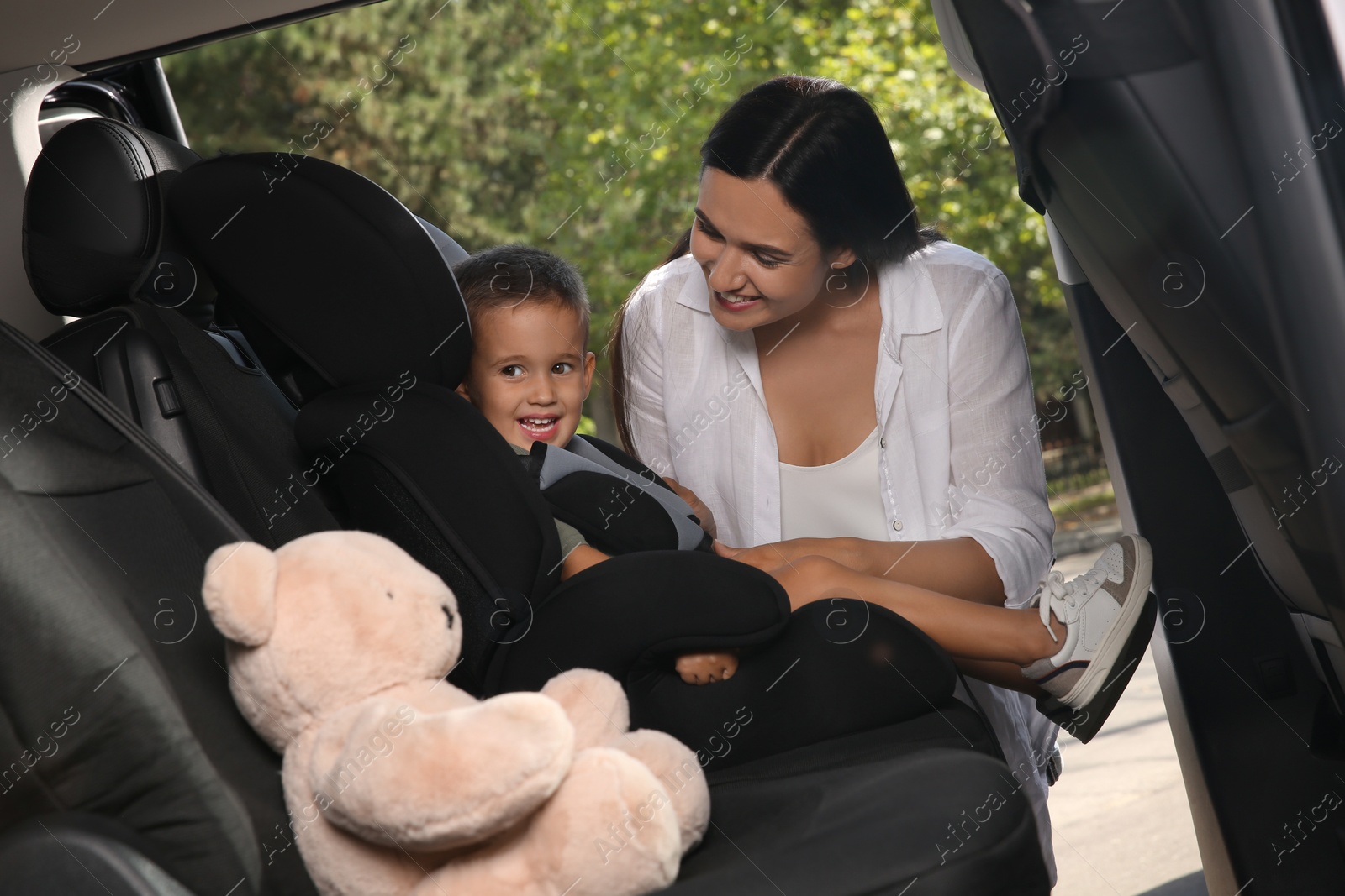 Photo of Mother fastening her son with car safety belt in child seat