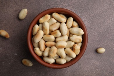 Photo of Roasted peanuts in bowl on brown table, top view