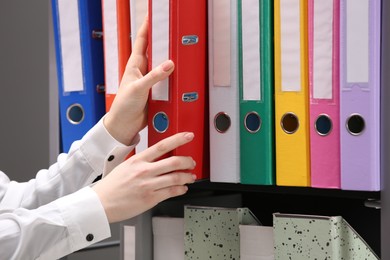 Woman taking folder with documents from shelf in office, closeup