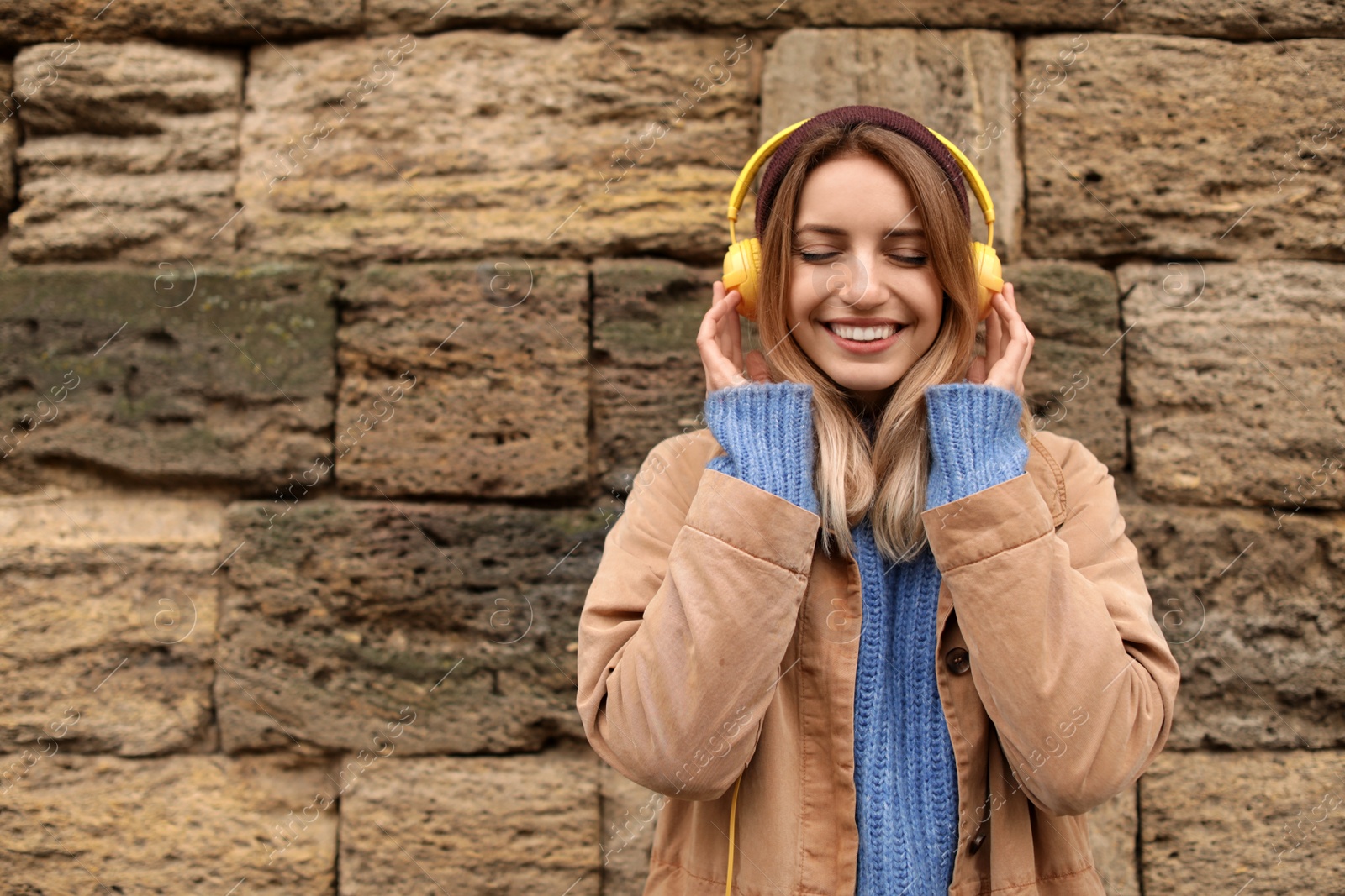 Photo of Young woman with headphones listening to music near stone wall. Space for text