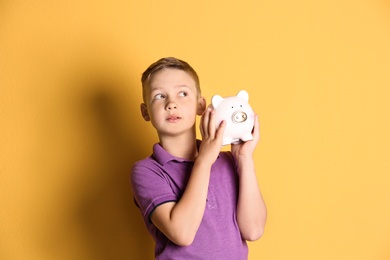 Little boy with piggy bank on color background