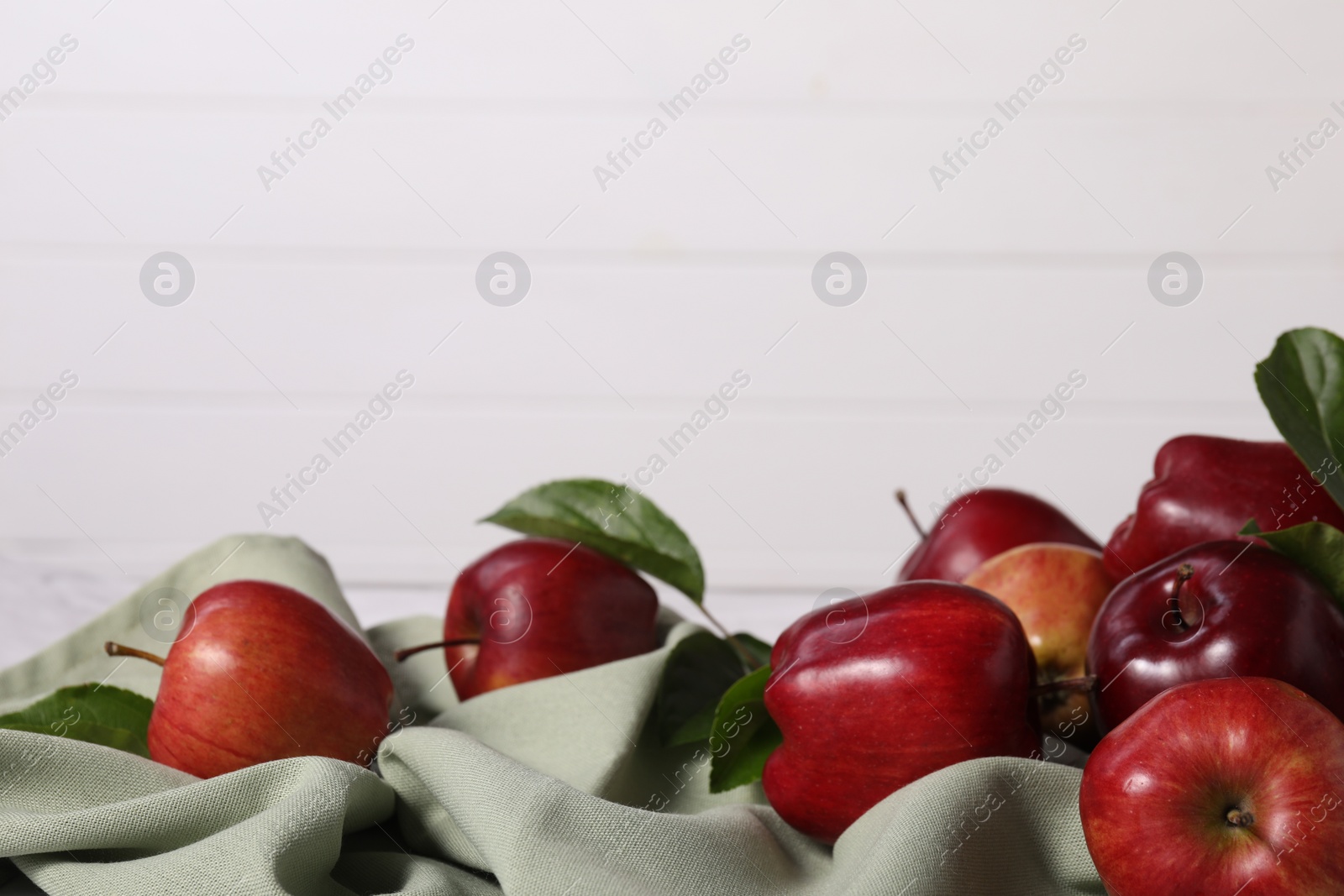 Photo of Fresh ripe red apples with leaves on table near white wall