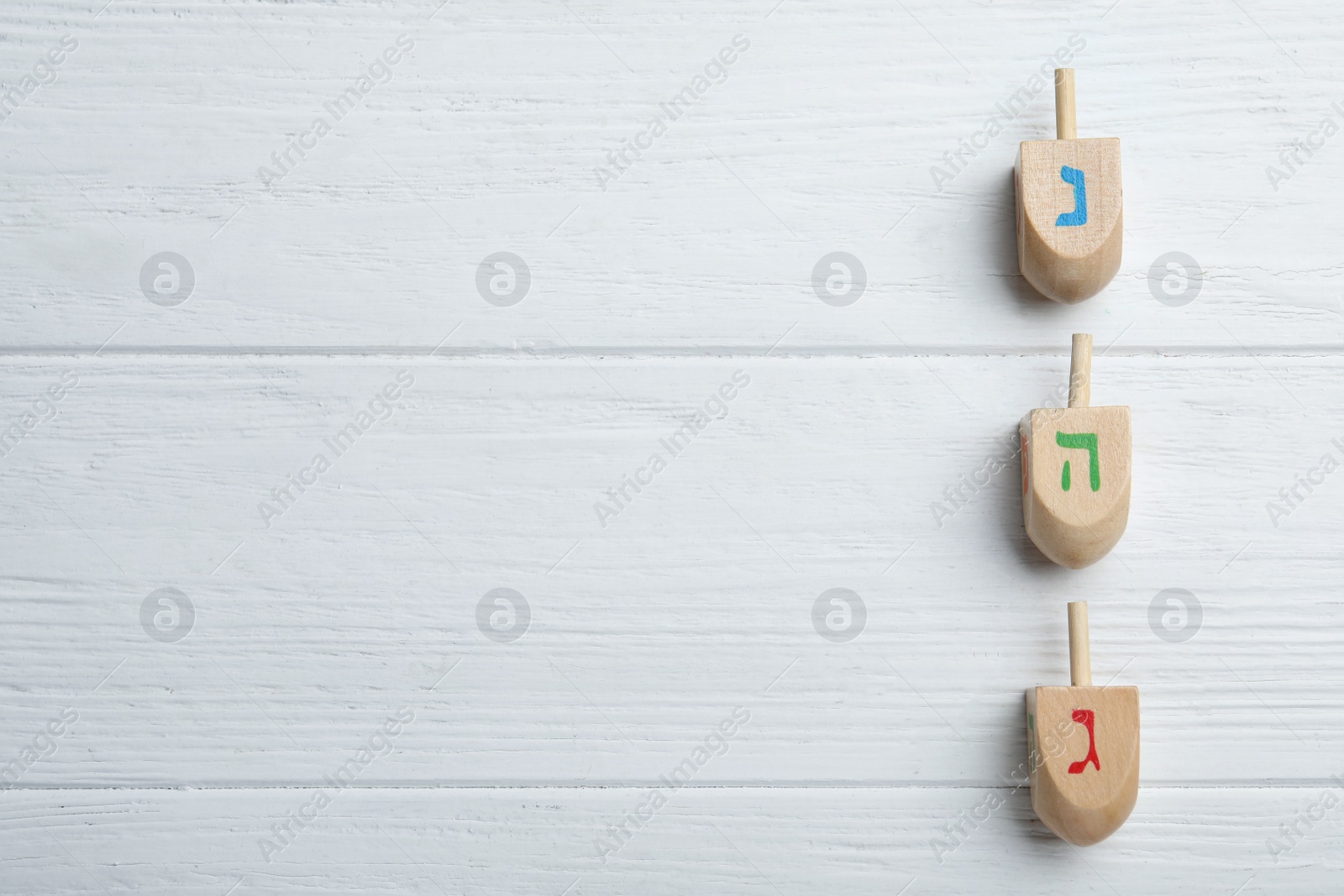 Photo of Hanukkah traditional dreidels with letters Nun, He and Gimel on white wooden table, flat lay. Space for text