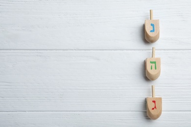 Photo of Hanukkah traditional dreidels with letters Nun, He and Gimel on white wooden table, flat lay. Space for text