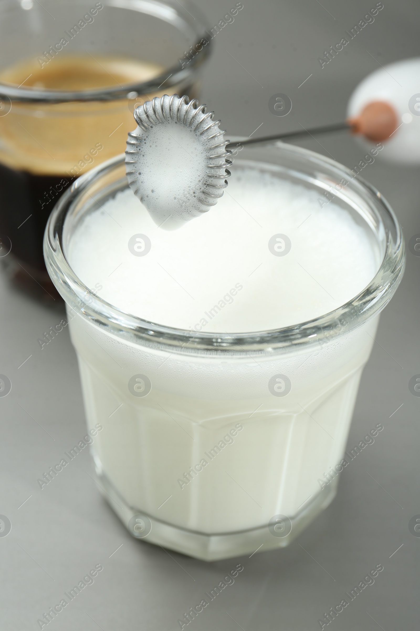 Photo of Mini mixer (milk frother), whipped milk and coffee in glasses on grey background, closeup