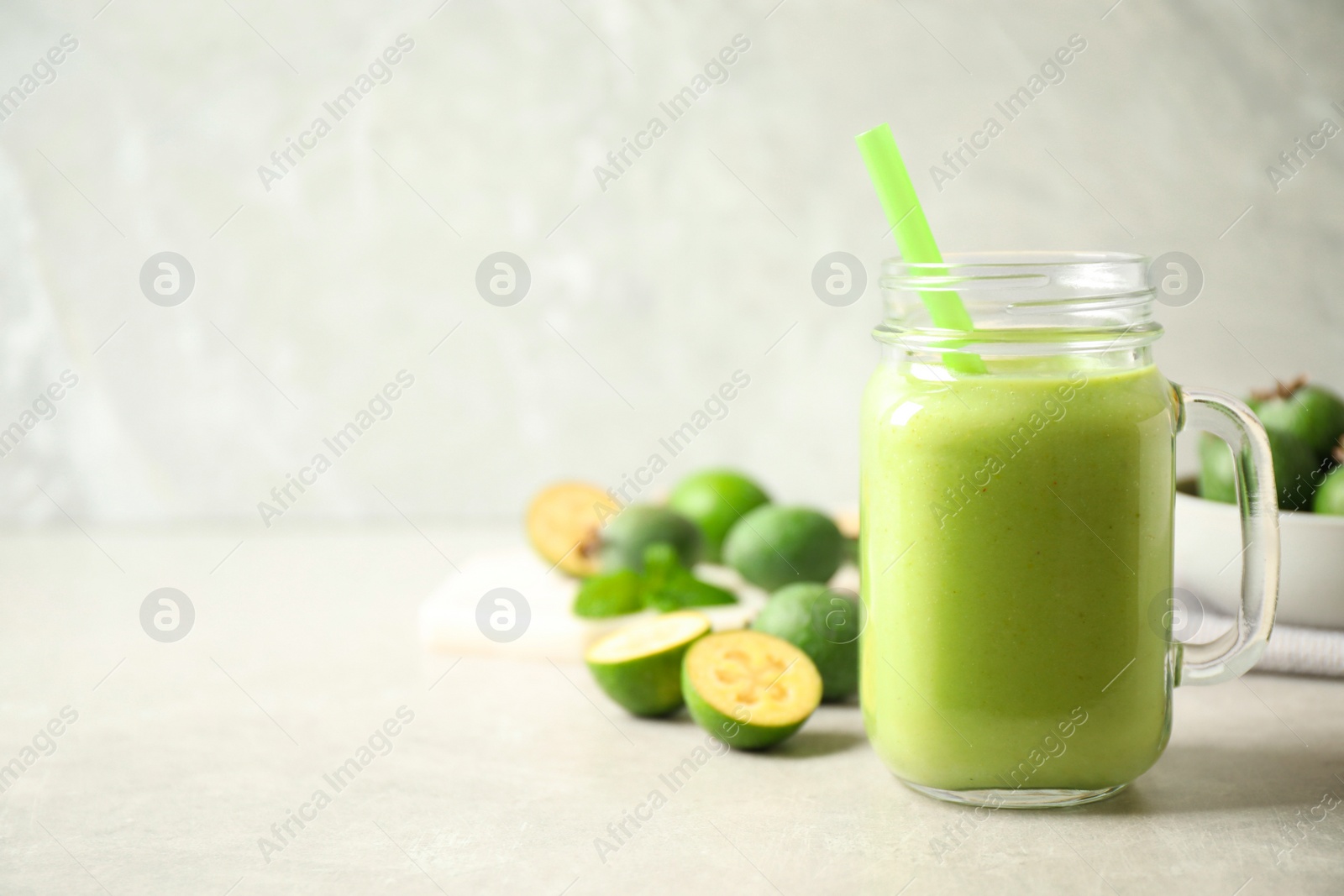 Photo of Fresh feijoa smoothie in mason jar on light table, closeup. Space for text