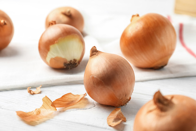 Photo of Ripe yellow onion bulbs on white wooden table, closeup