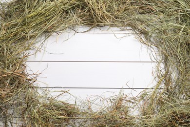 Frame made of dried hay on white wooden table, top view. Space for text