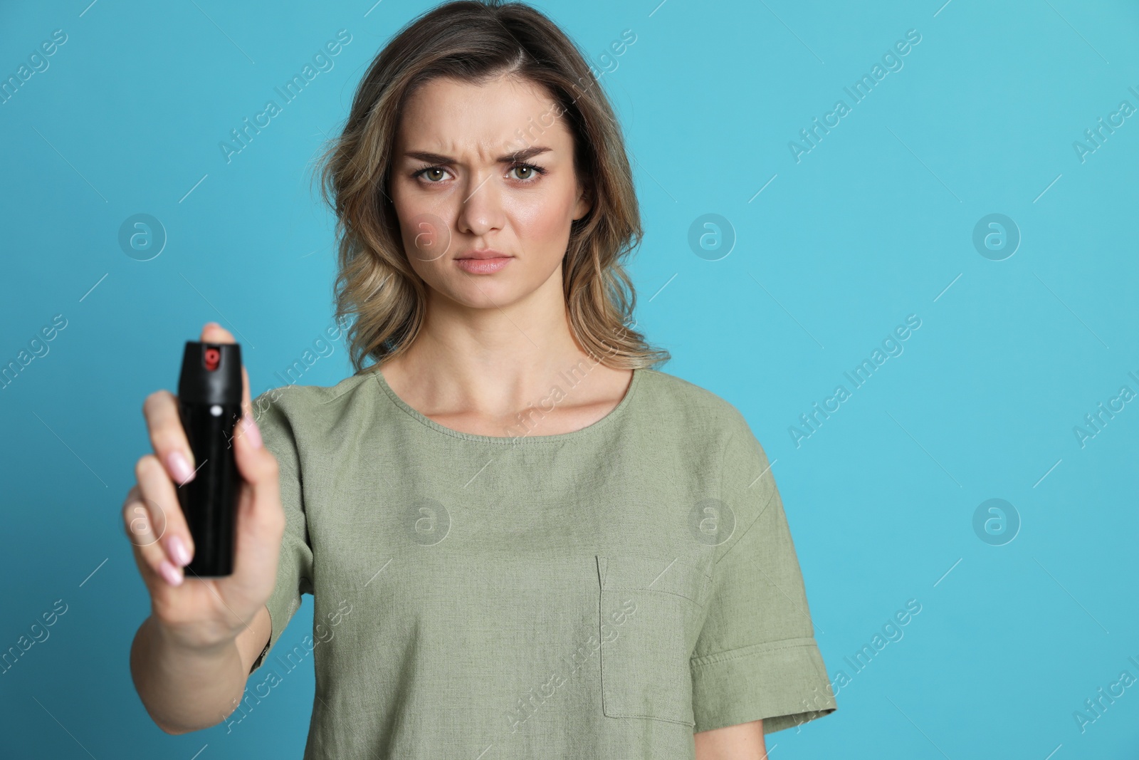 Photo of Young woman using pepper spray on turquoise background