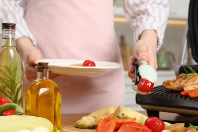 Woman cooking different products with electric grill at wooden table in kitchen, closeup