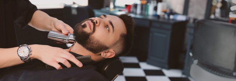 Professional hairdresser working with bearded client in barbershop, space for text. Banner design