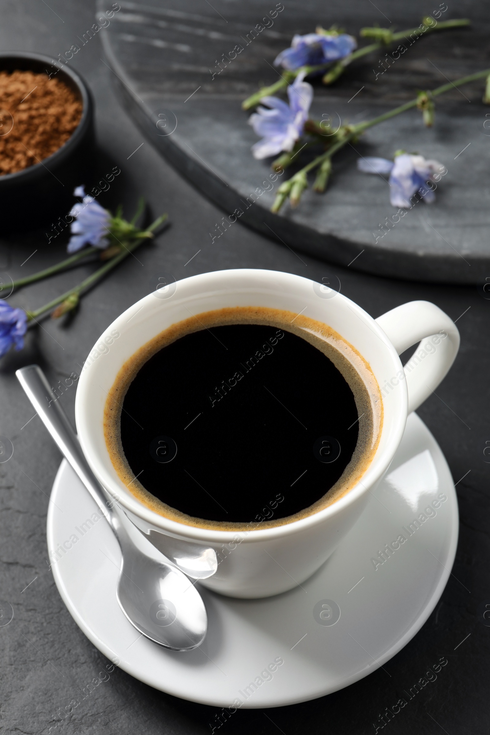 Photo of Cup of delicious chicory drink and flowers on black table