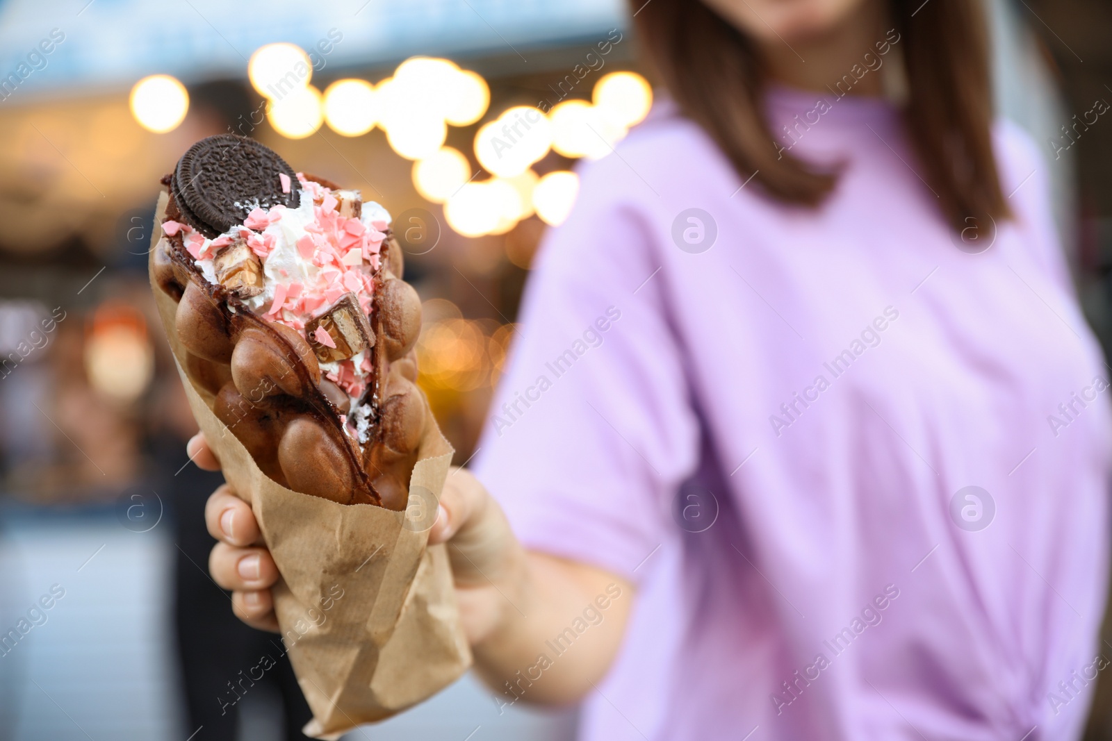 Photo of Young woman holding delicious sweet bubble waffle with ice cream outdoors, closeup