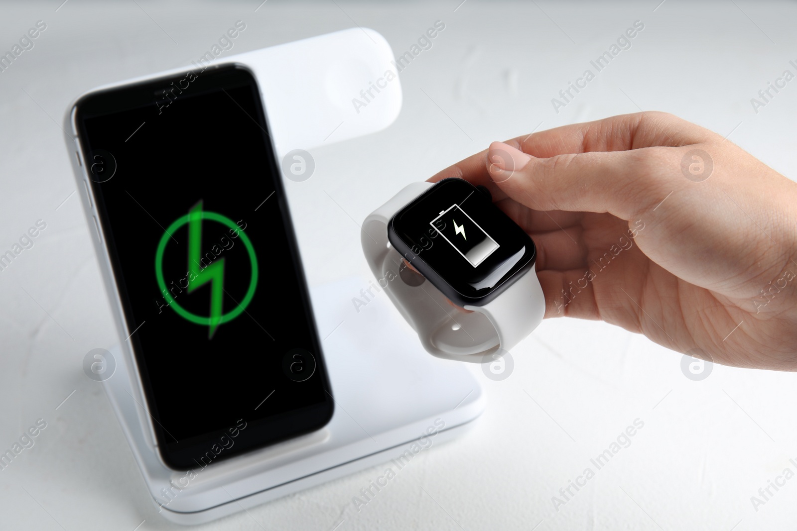 Photo of Woman putting smartwatch onto wireless charger at white stone table, closeup