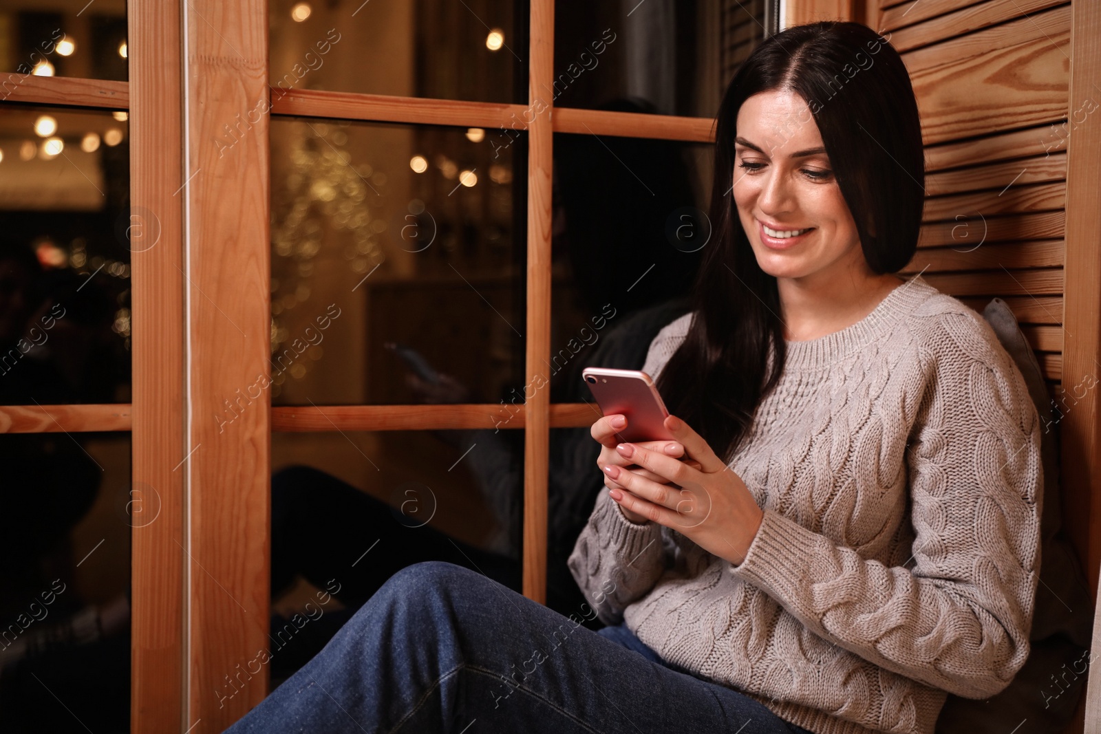 Photo of Beautiful woman using mobile phone near window indoors. Christmas celebration