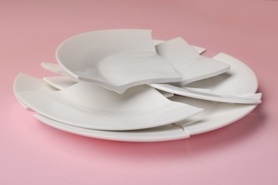 Photo of Pieces of broken ceramic plate on pink background, closeup