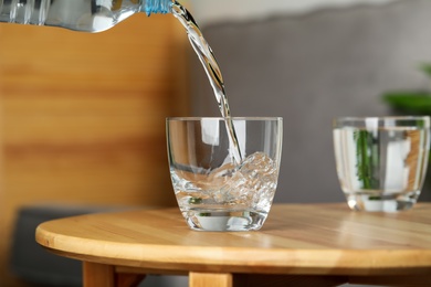 Photo of Pouring water from bottle into glass on wooden table indoors, space for text. Refreshing drink