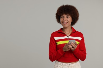 Happy young woman with smartphone on grey background. Space for text