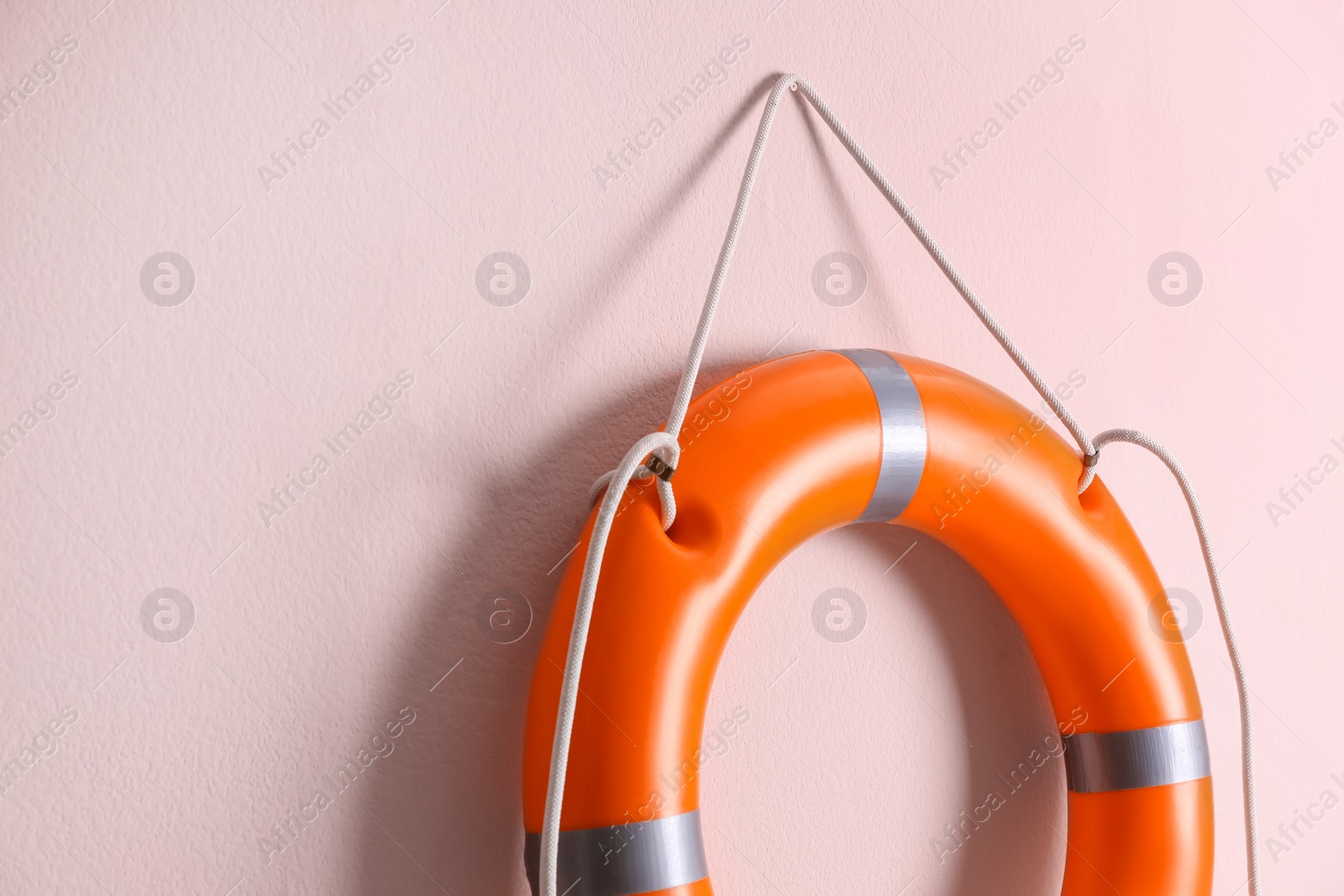 Photo of Orange lifebuoy and space for text on pink background. Rescue equipment