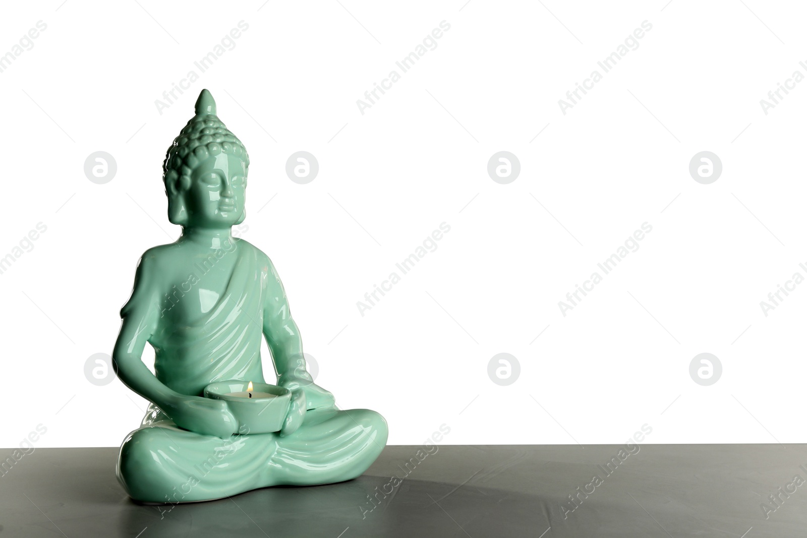 Photo of Beautiful ceramic Buddha sculpture with burning candle on table against grey background. Space for text