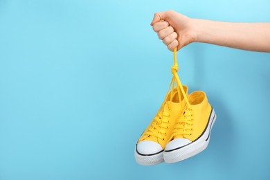 Photo of Woman holding pair of sneakers on light blue background, closeup. Space for text