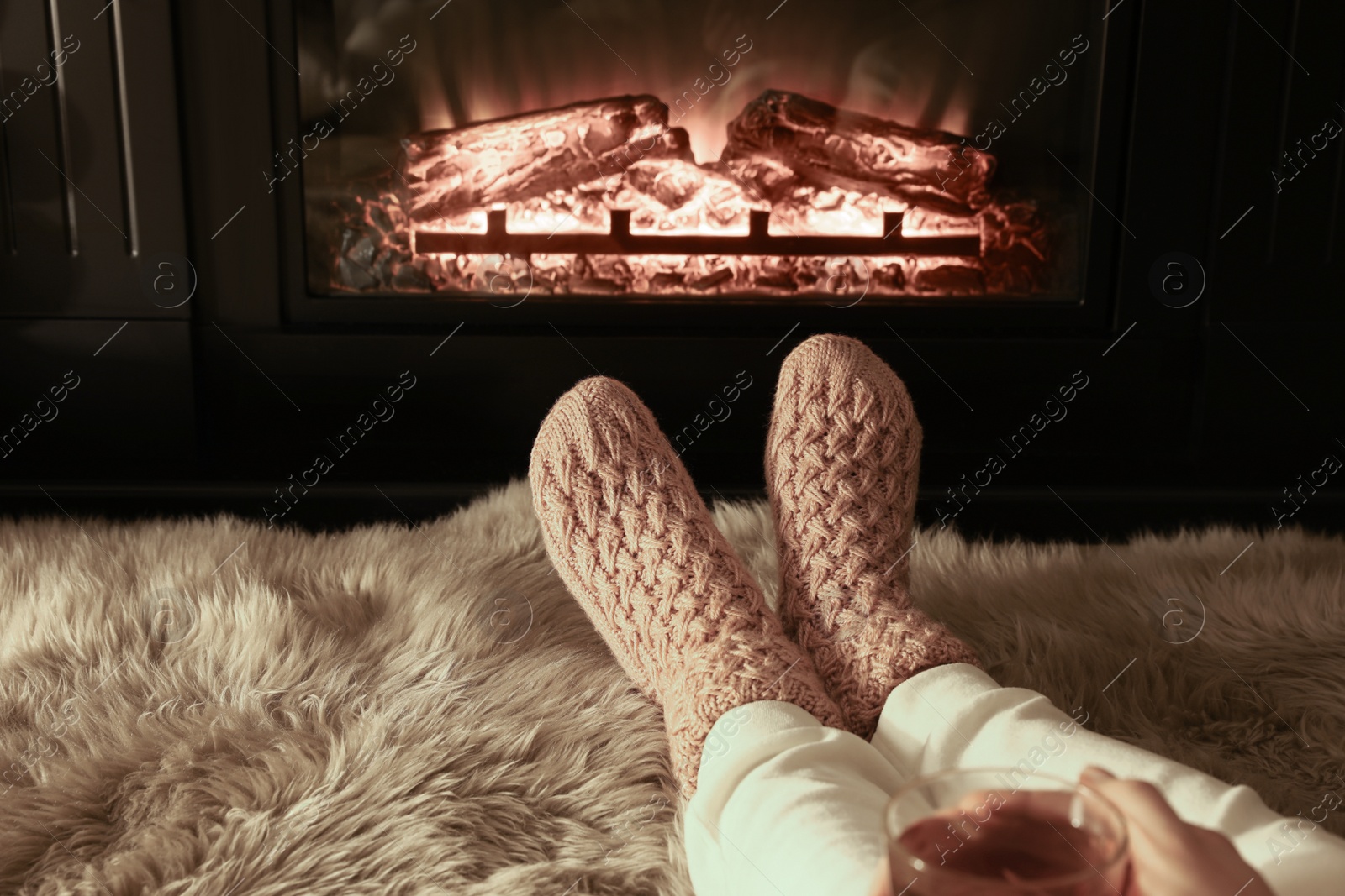 Photo of Woman in knitted socks resting near fireplace at home, closeup of legs