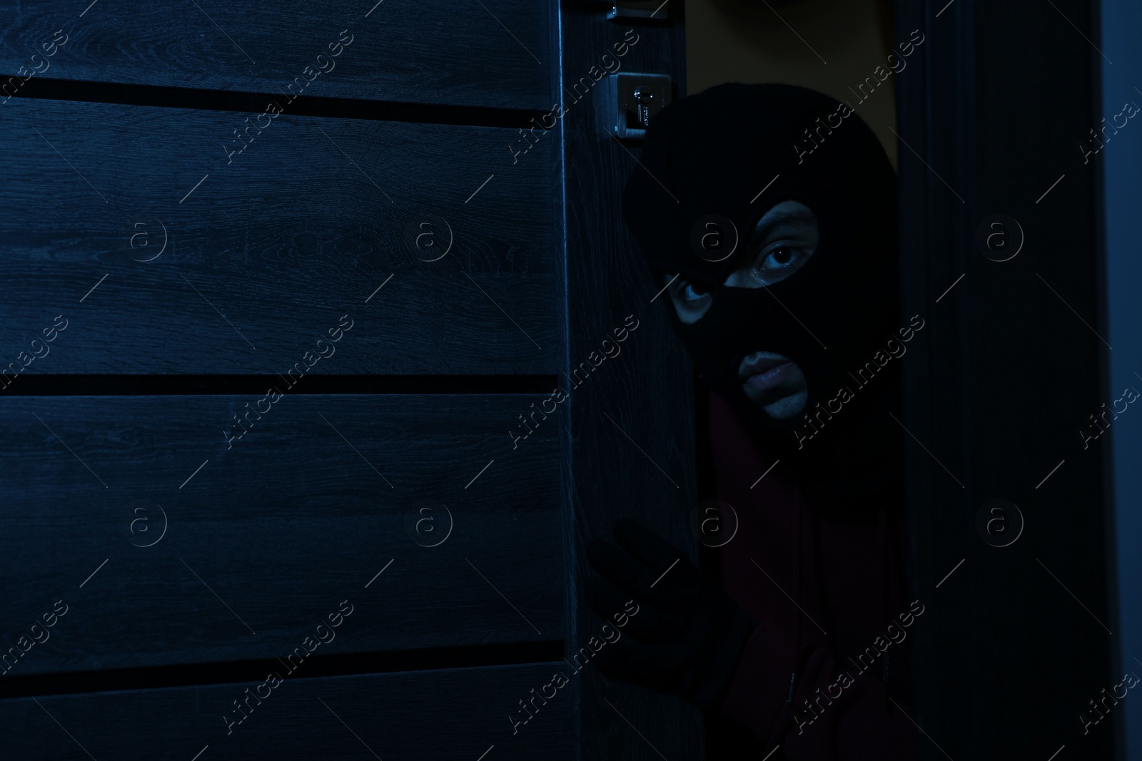 Photo of Thief in balaclava entering foreign house at night. Burglary