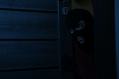 Thief in balaclava entering foreign house at night. Burglary