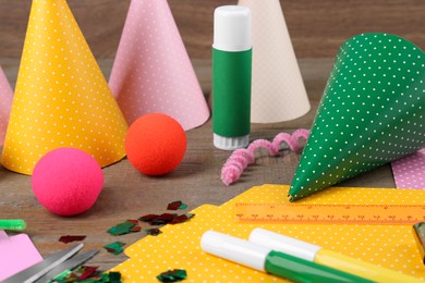 Photo of Different stationery and materials for creation of colorful party hats on wooden table. Handmade decorations