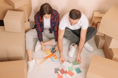 Photo of Happy couple surrounded by moving boxes choosing colors in new apartment, above view