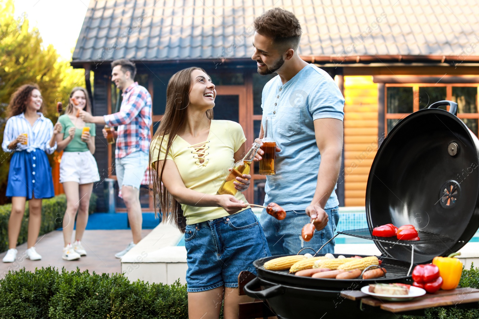 Photo of Young man and woman with grilled sausages at barbecue party outdoors