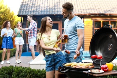 Young man and woman with grilled sausages at barbecue party outdoors