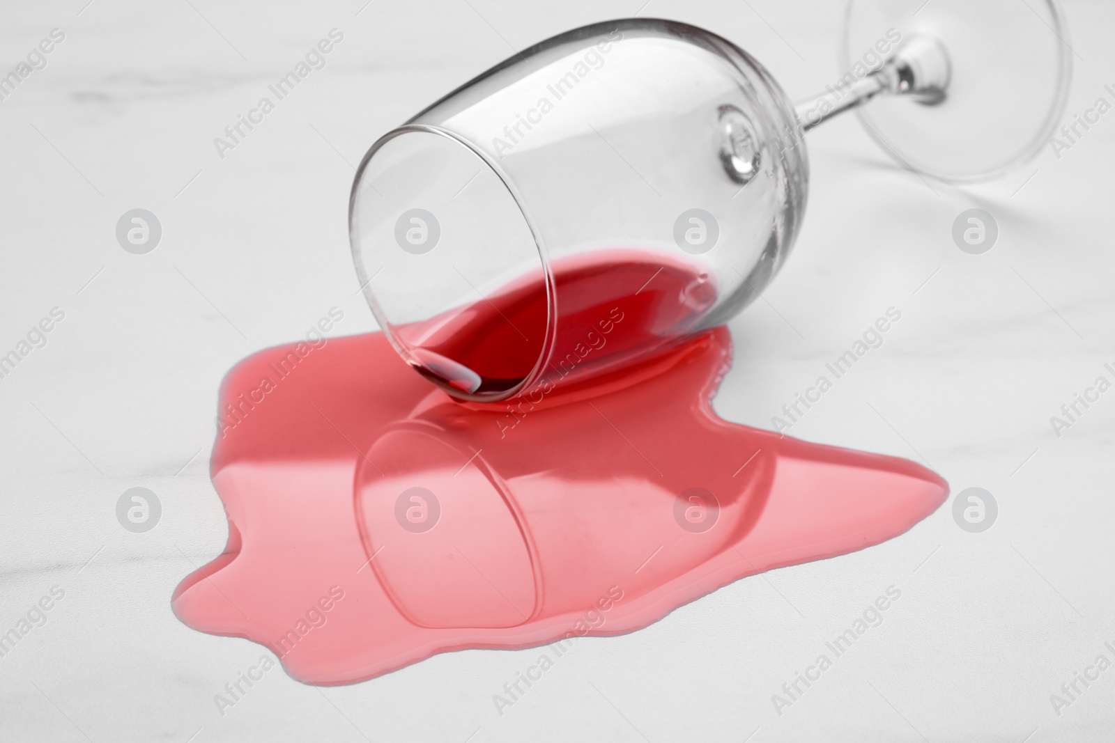 Photo of Glass with spilled red wine on white marble surface, closeup