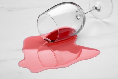 Glass with spilled red wine on white marble surface, closeup