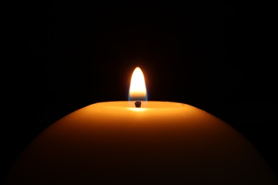Photo of Burning wax candle on black background, closeup