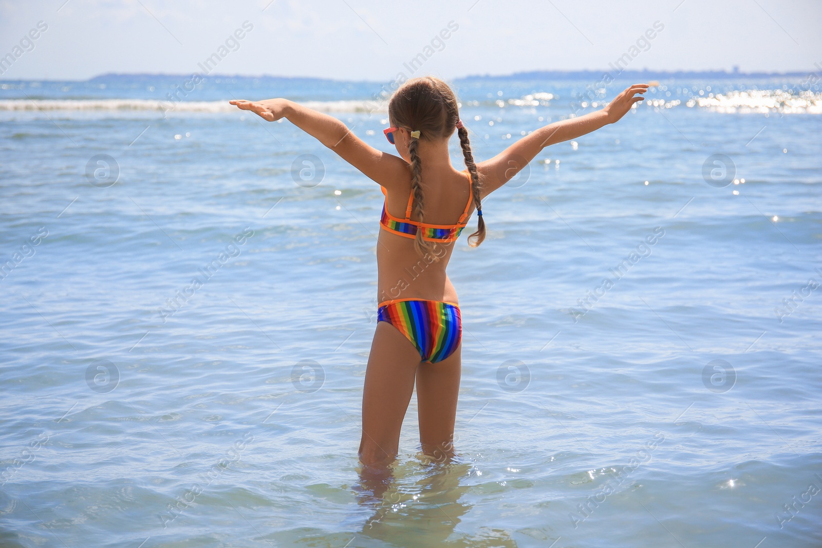 Photo of Little girl having fun in sea on sunny day. Beach holiday