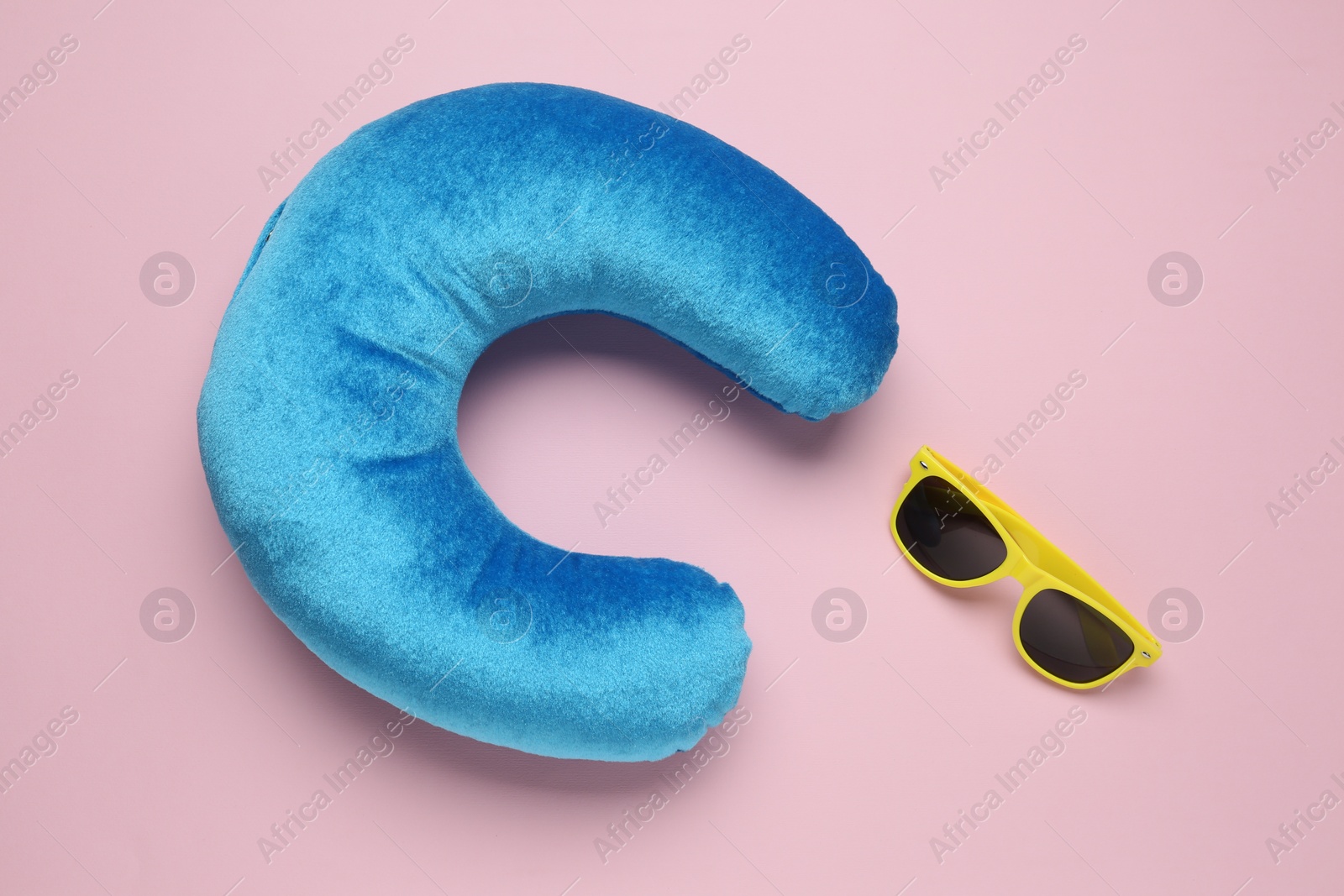 Photo of Light blue travel pillow and sunglasses on pink background, flat lay