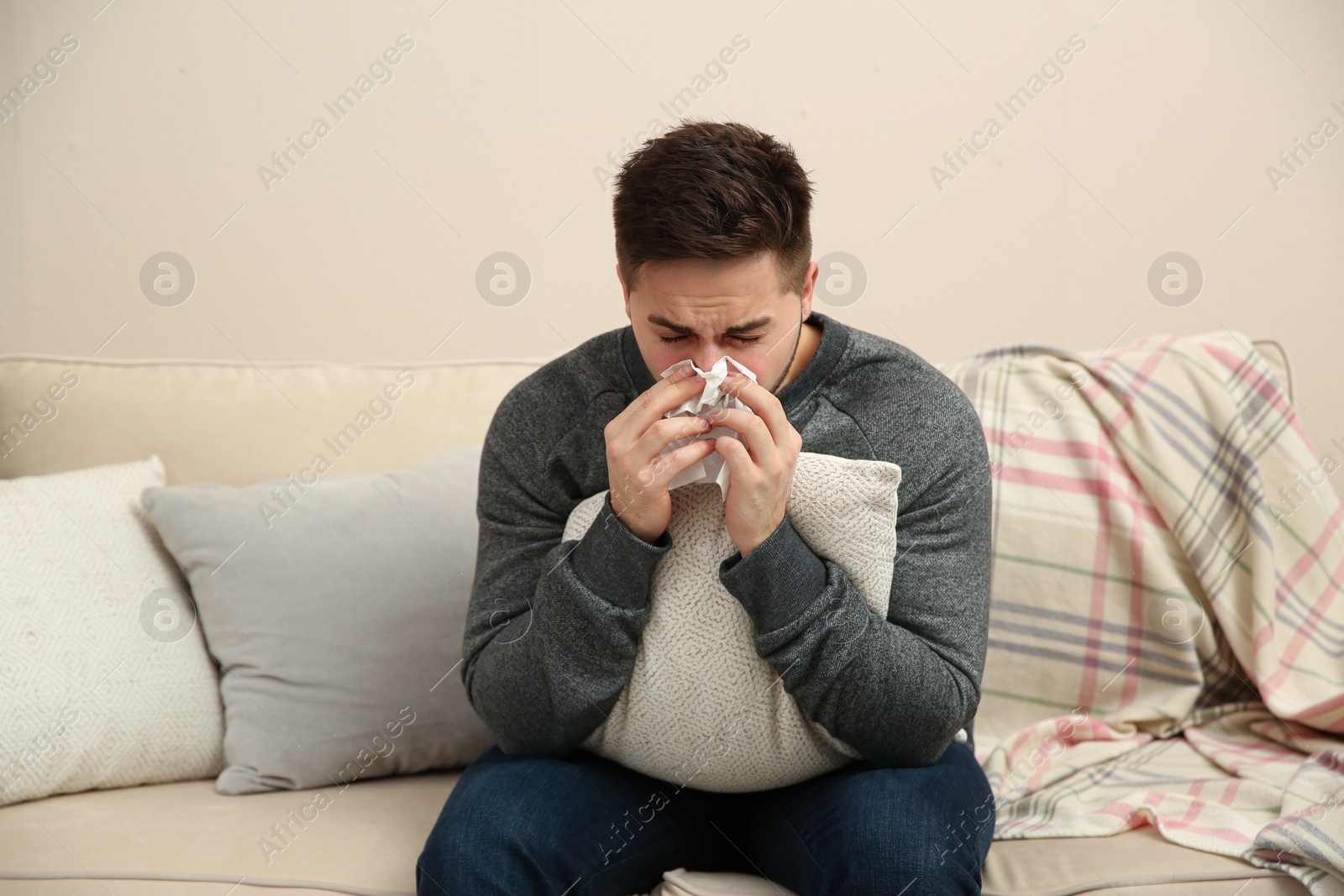 Photo of Sick young man sneezing at home. Influenza virus