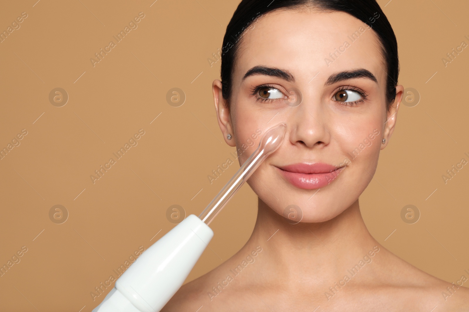 Photo of Woman using high frequency darsonval device on beige background. Space for text