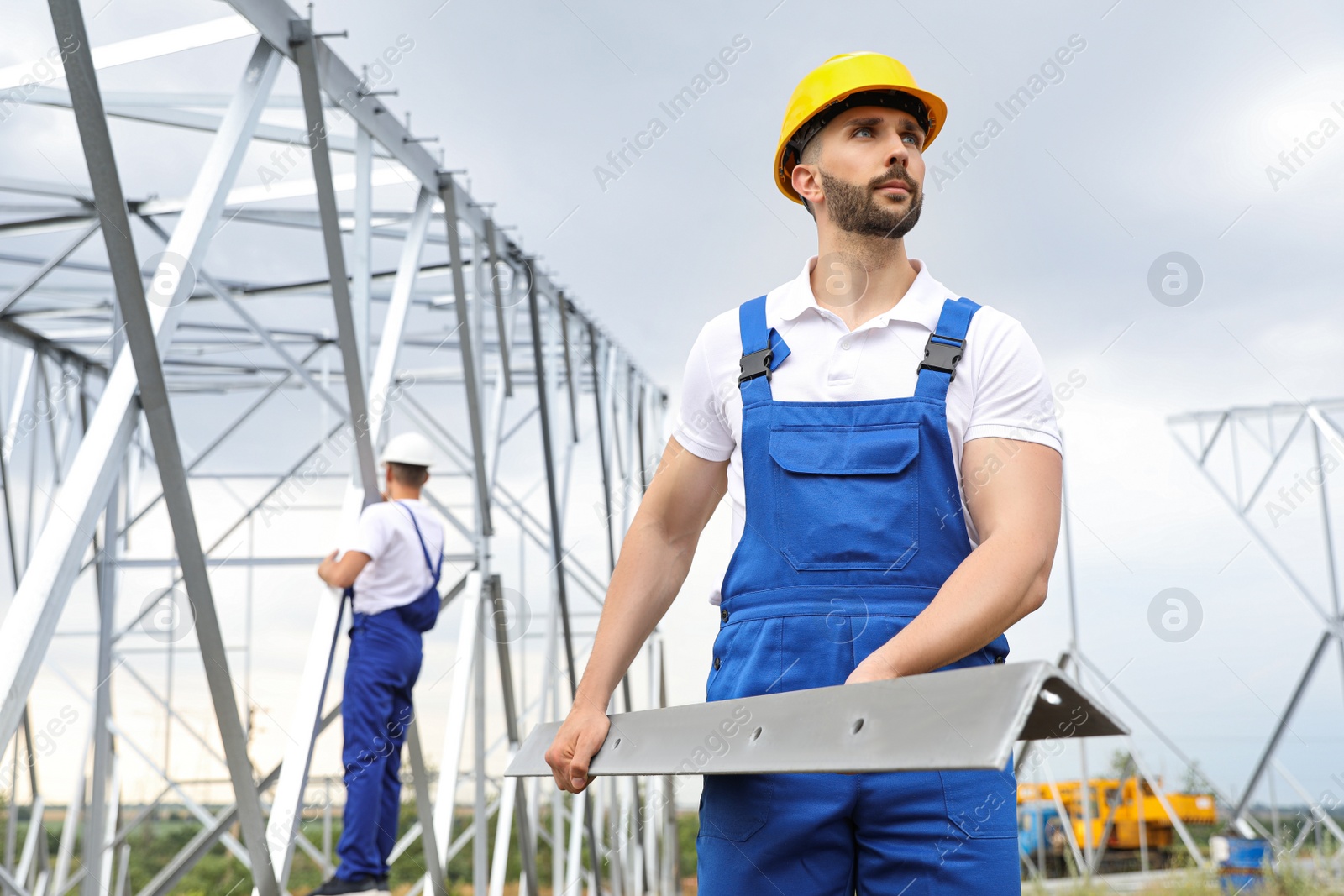 Photo of Workers building high voltage tower construction outdoors. Installation of electrical substation