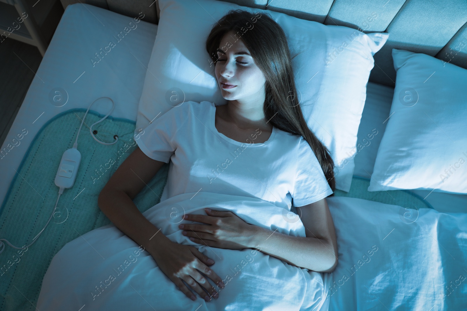 Photo of Young woman sleeping on electric heating pad in bed at night, top view